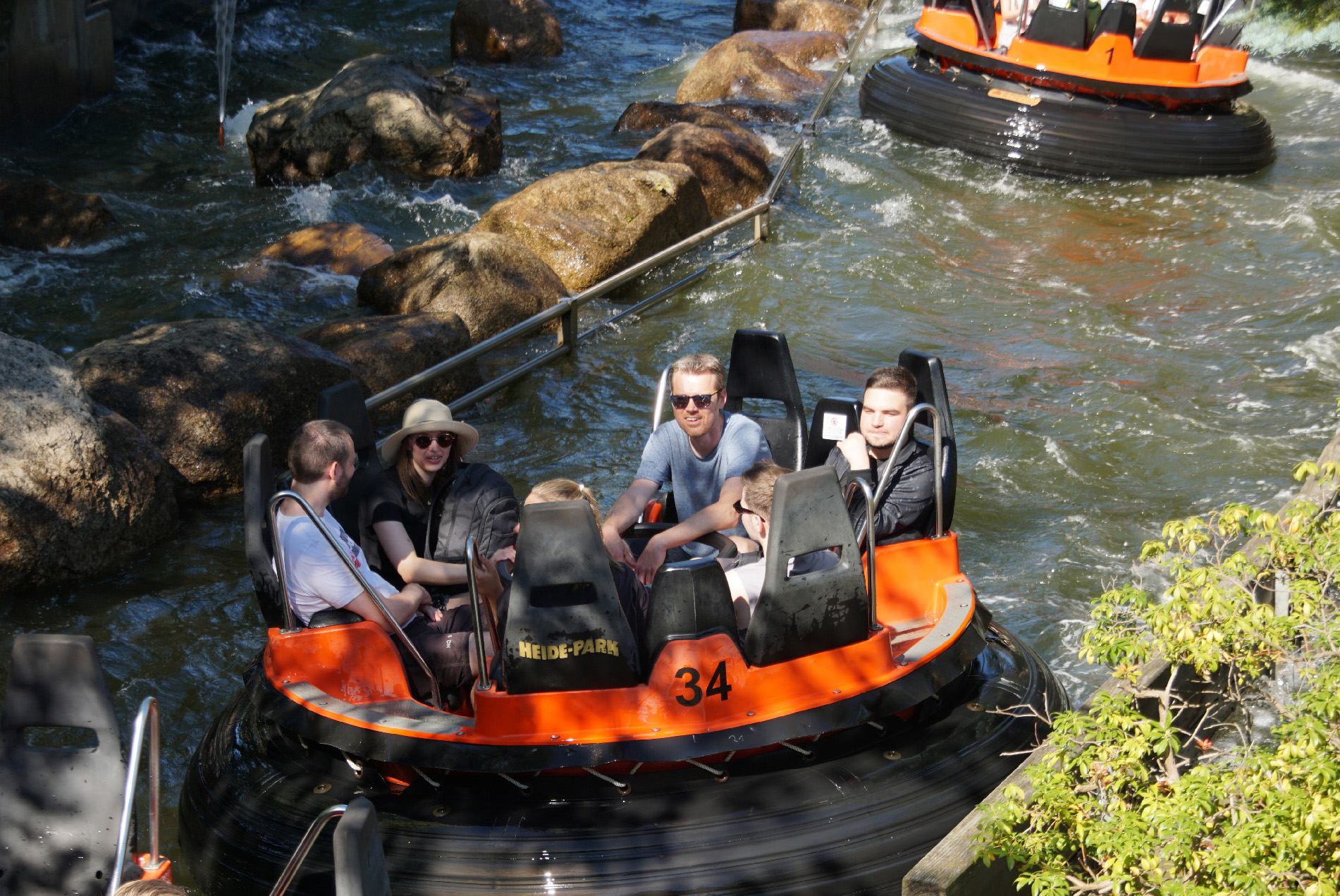 Vier Personen fahren gemeinsam in einem orangefarbenen Rundboot durch eine wilde Wasserbahn im Heide Park.